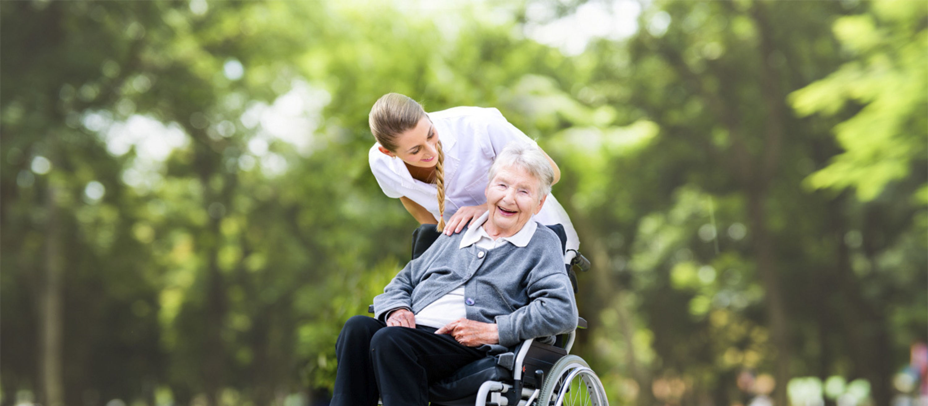 Lachende Pensionistin im Rollstuhl mit Pflegerin.