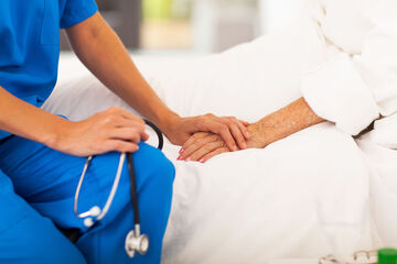Arzt sitzt am Bett einer älteren Patientin und hält ihre Hand.